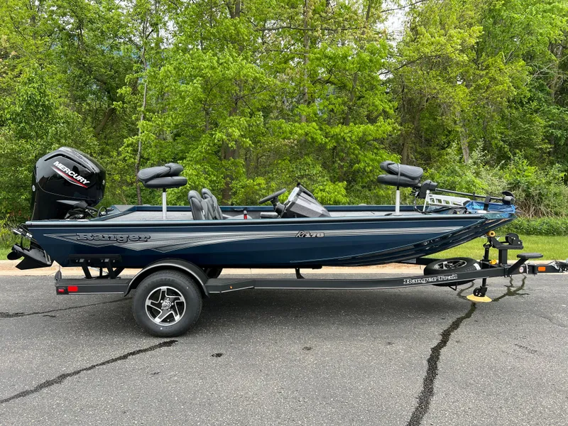 The Image of 2025 Ranger RT178 boat on trailer, parked on asphalt, surrounded by lush green trees. - 0