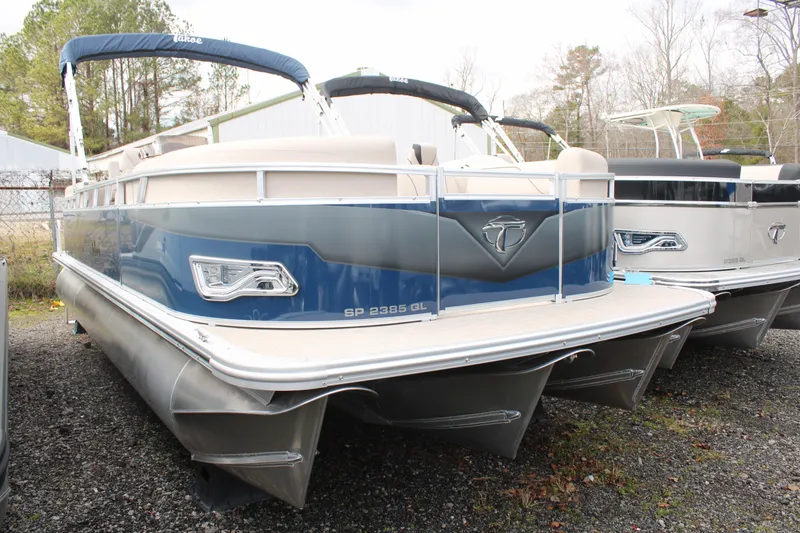 Slide: The Image of 2024 Tahoe Pontoon Sport 2385 QL, blue and white, docked on gravel lot. - 1