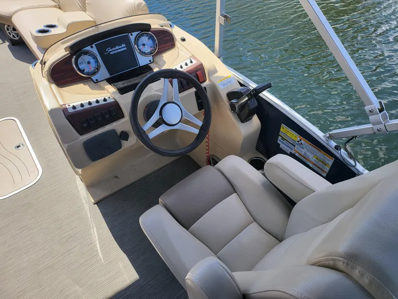 Slide: The Image of 2017 Godfrey Sweetwater 215c boat interior with steering wheel and dashboard, on calm water. - 10