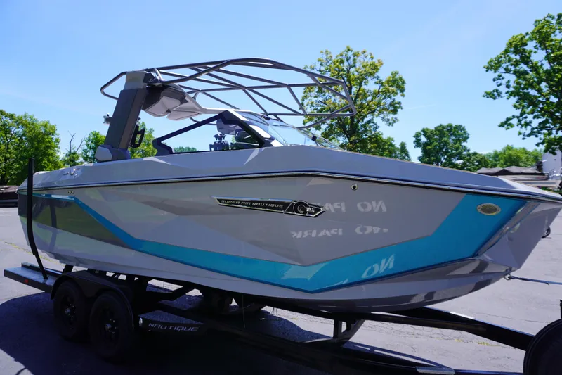 The Image of 2025 Nautique Super Air Nautique G21 boat on trailer, sleek design, blue accents, sunny day. - 0
