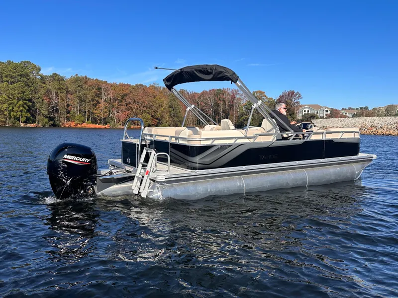 Slide: The Image of 2025 Tahoe Pontoon Sport 85 Quad Lounger on a lake, featuring a Mercury outboard motor. - 2