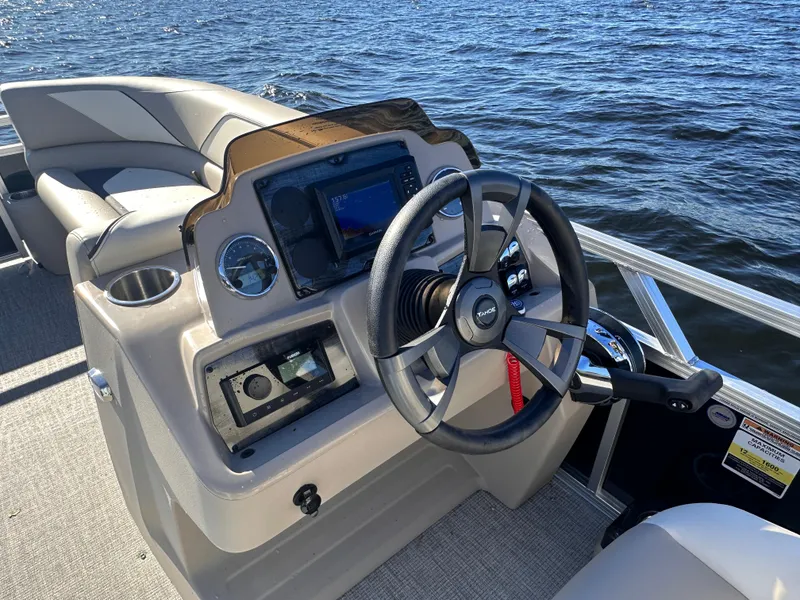Slide: The Image of 2025 Tahoe Pontoon Sport 85 Quad Lounger dashboard with steering wheel, on a lake. - 3