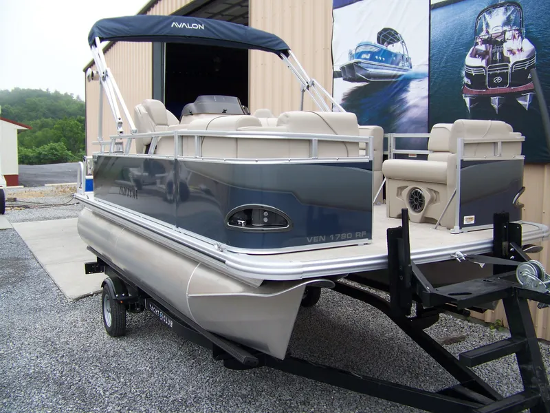 Slide: The Image of 2025 Avalon Venture Rear Fish pontoon boat on trailer, parked outside a building. - 3