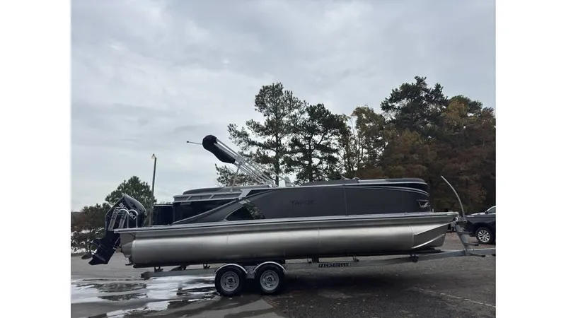 Slide: The Image of 2025 Tahoe Pontoon LTZ Quad Lounger on trailer, parked outdoors under cloudy sky. - 2