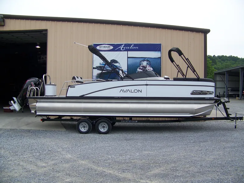 The Image of 2025 Avalon Catalina Cruise Rear Bench Windshield pontoon boat on trailer outside a warehouse. - 0