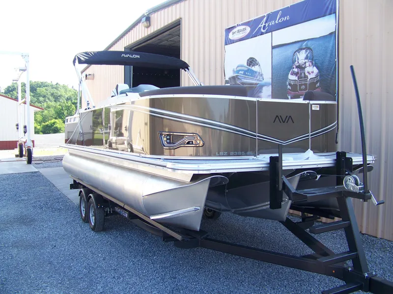 Slide: The Image of 2025 Avalon LSZ ELITE pontoon boat on trailer outside a warehouse. - 3