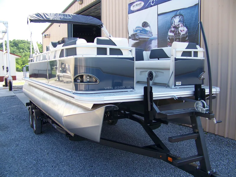 Slide: The Image of 2025 Avalon VENTURE QUAD LOUNGER pontoon boat on trailer, parked outside a building. - 4