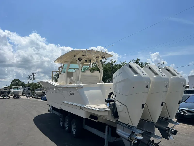 Slide: The Image of 2025 Scout 357 LXF boat with triple engines on a trailer under a blue sky. - 2