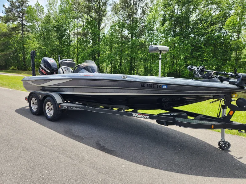Slide: The Image of 2018 Triton 20 TRX boat on trailer, parked on road with lush green trees in background. - 1