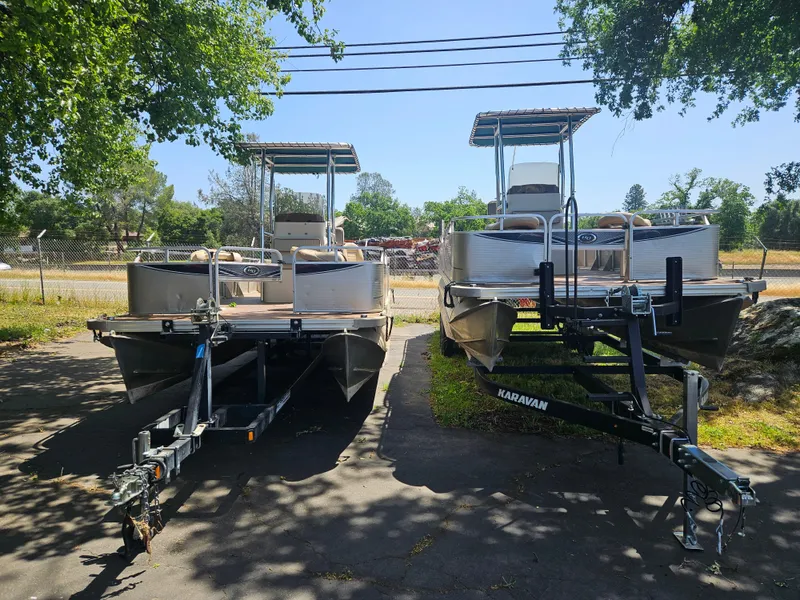 Slide: The Image of 2019 Apex Marine ANGERQWEST pontoon boats on trailers, parked outdoors under trees. - 7