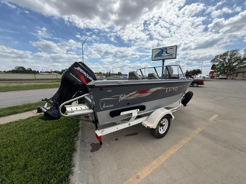 Slide: The Image of 2002 Lund 1800 Fisherman boat with Mercury outboard motor on a trailer, parked outdoors. - 4