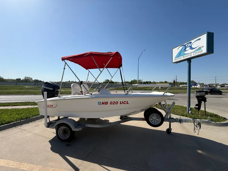 Slide: The Image of 2009 Boston Whaler 130 Super Sport boat with red canopy on trailer, parked near dealership sign. - 8
