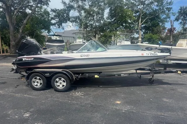 Slide: The Image of 2002 Triton 190-FS boat on trailer, parked outdoors with trees in the background. - 1