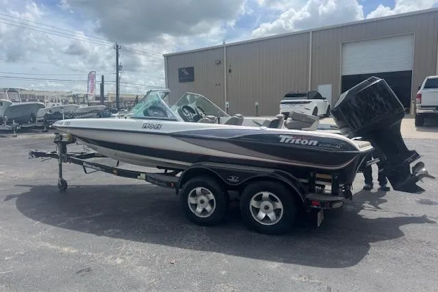 Slide: The Image of 2002 Triton 190-FS boat on trailer, parked outdoors near industrial building. - 5