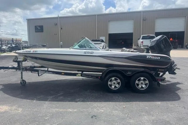 Slide: The Image of 2002 Triton 190-FS boat on trailer, parked outside a warehouse under cloudy sky. - 6