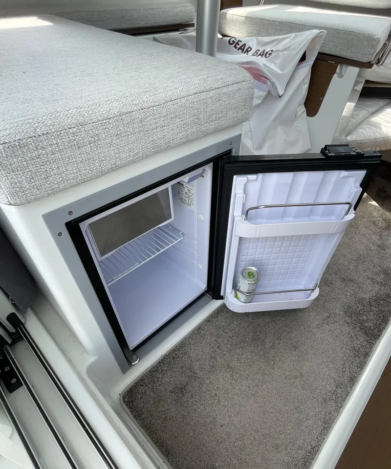 Slide: The Image of 2022 Jeanneau NC 695 Series 2 interior with compact refrigerator and cushioned seating. - 10