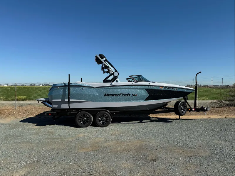 Slide: The Image of 2024 MasterCraft XStar S boat on trailer, parked outdoors under clear blue sky. - 0
