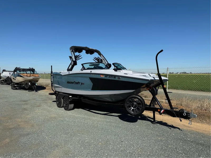 Slide: The Image of 2024 MasterCraft XStar S boat on trailer, parked outdoors under clear blue sky. - 1