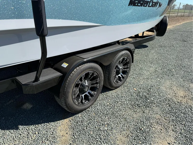 Slide: The Image of 2024 MasterCraft XStar S boat on a dual-axle trailer, parked on gravel. - 11