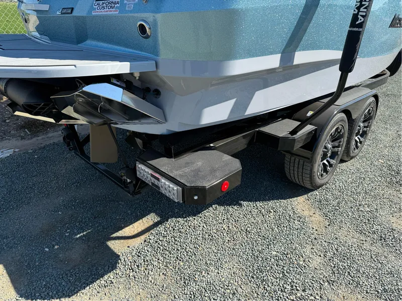 Slide: The Image of 2024 MasterCraft XStar S boat on a trailer, rear view, parked on gravel. - 12