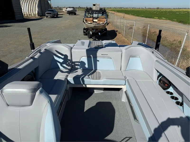 Slide: The Image of 2024 MasterCraft XStar S boat interior with gray and blue seating, parked outdoors. - 21