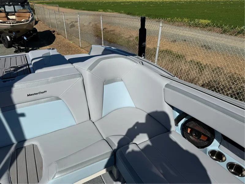 Slide: The Image of 2024 MasterCraft XStar S boat interior with gray and blue seating, near a fence. - 22