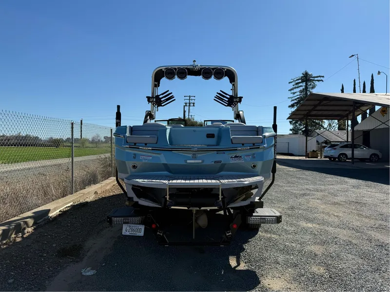 Slide: The Image of 2024 MasterCraft XStar S boat, rear view, parked outdoors on gravel, under clear blue sky. - 5