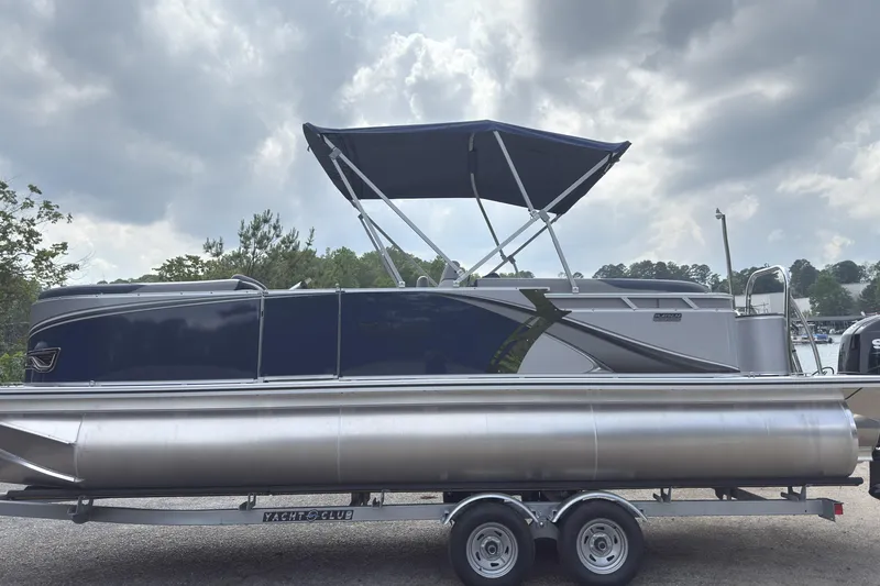 Slide: The Image of 2025 Tahoe LTZ Quad Lounger 23 pontoon boat on trailer, under cloudy sky. - 0