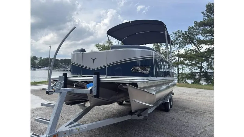Slide: The Image of 2025 Tahoe LTZ Quad Lounger 23 pontoon boat on trailer, parked near a lake. - 10