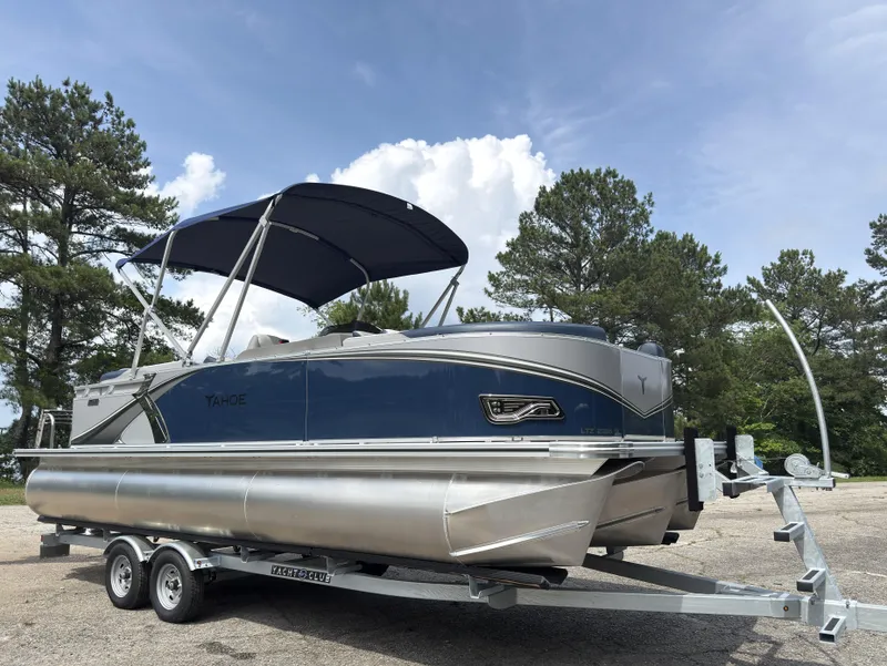 Slide: The Image of 2025 Tahoe LTZ Quad Lounger 23 pontoon boat on trailer, parked outdoors. - 2