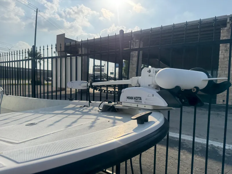 Slide: The Image of 2013 Shallow Sport 21 Sport boat with Minn Kota trolling motor, parked near a fence. - 2