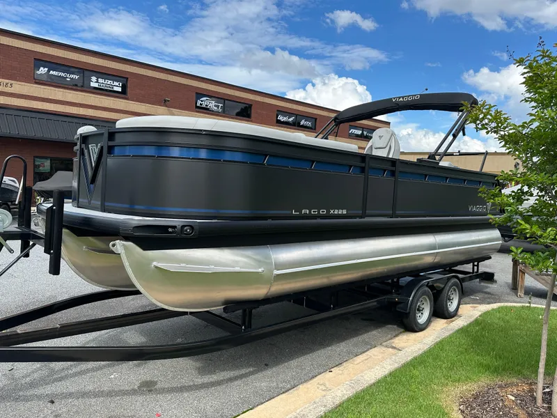 Slide: The Image of 2025 Viaggio Lago X-S pontoon boat on trailer, parked outdoors under a blue sky. - 0
