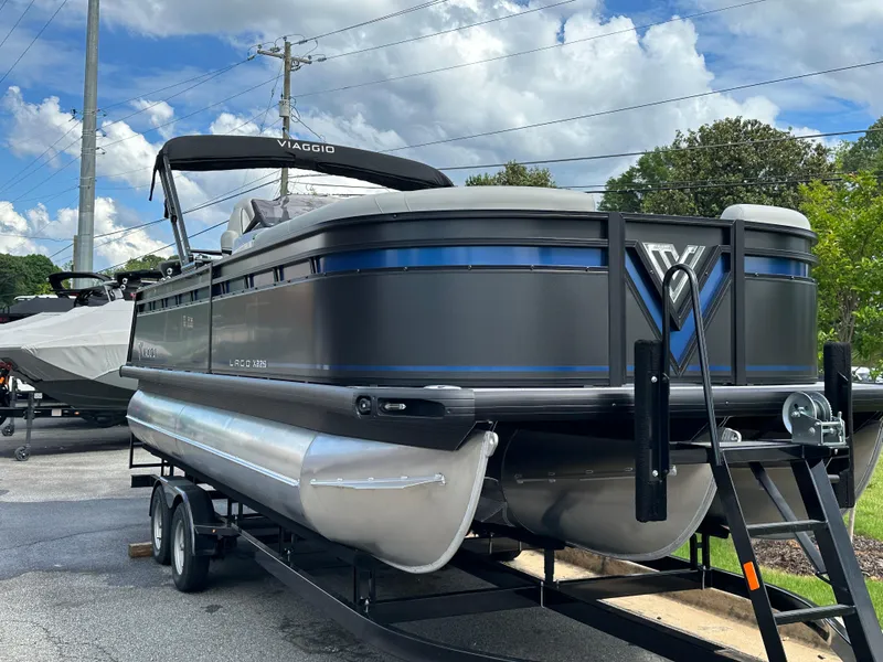 Slide: The Image of 2025 Viaggio Lago X-S pontoon boat on trailer, parked outdoors under a cloudy sky. - 5