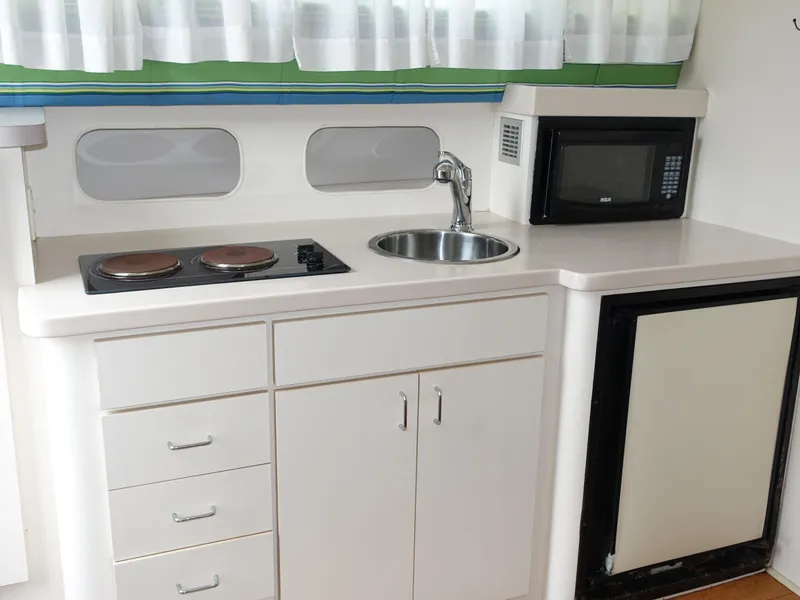 Slide: The Image of Compact kitchen area in a 1998 Mainship 31 Sedan Bridge boat, featuring stove, sink, and microwave. - 11
