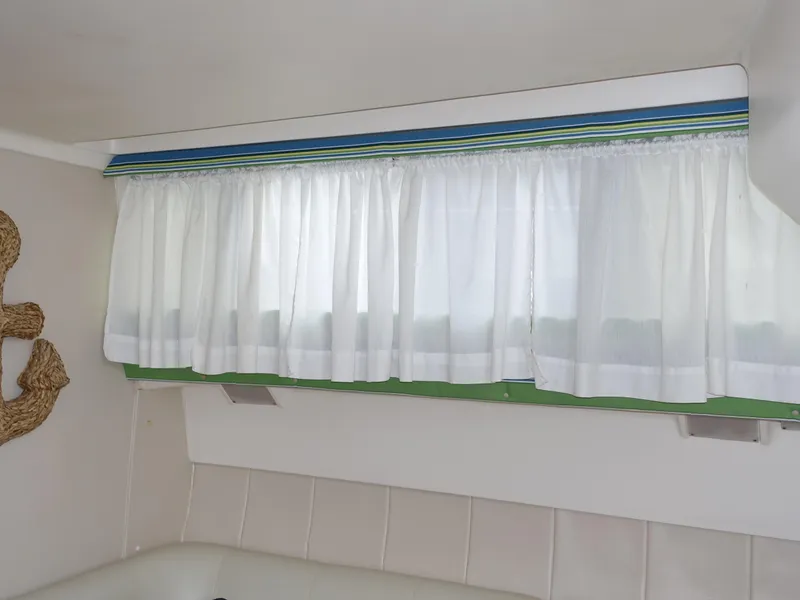 Slide: The Image of 1998 Mainship 31 Sedan Bridge interior with white curtains and decorative anchor. - 15