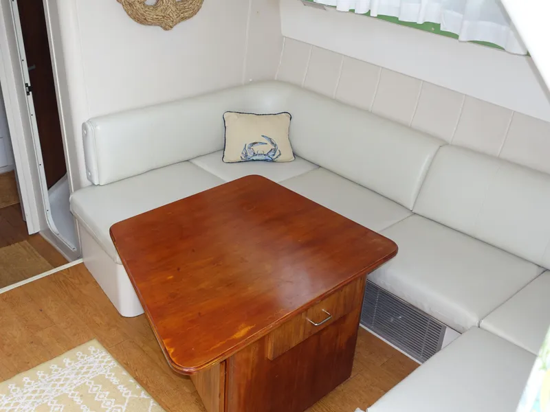 Slide: The Image of 1998 Mainship 31 Sedan Bridge interior with white seating and wooden table. - 16
