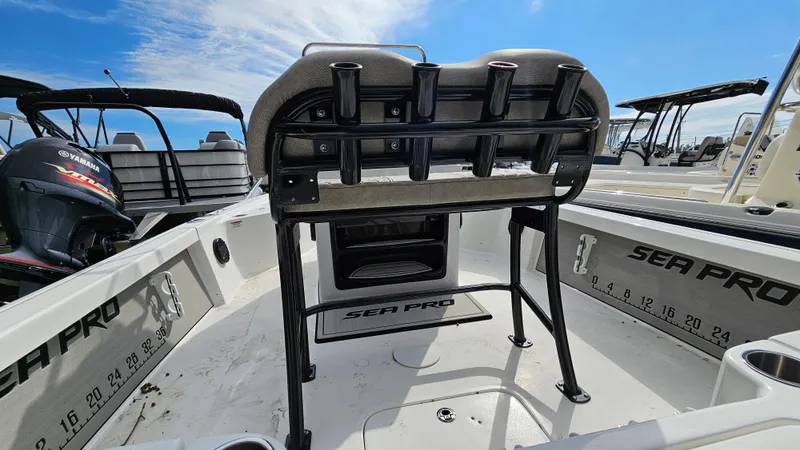 Slide: The Image of 2024 Sea Pro 210 Bay boat interior with seating and rod holders under a clear blue sky. - 13
