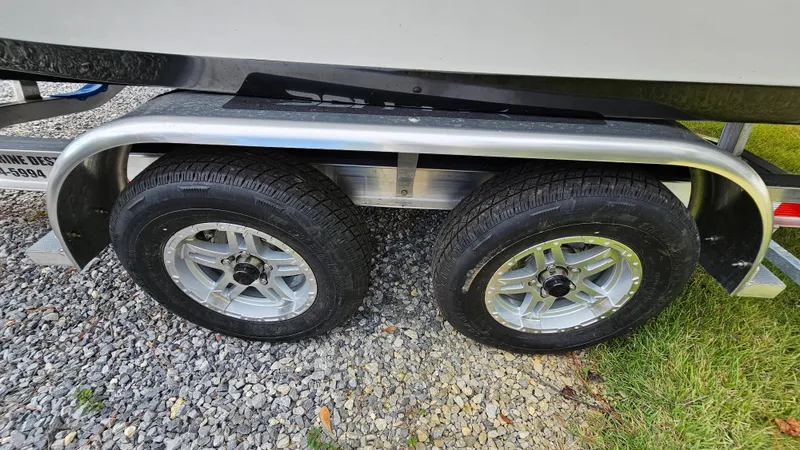 Slide: The Image of Trailer wheels of a 2024 Sea Pro 210 Bay boat on gravel and grass. - 21