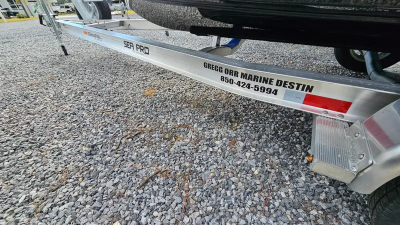 Slide: The Image of 2024 Sea Pro 210 Bay boat trailer on gravel, featuring dealership contact details. - 22