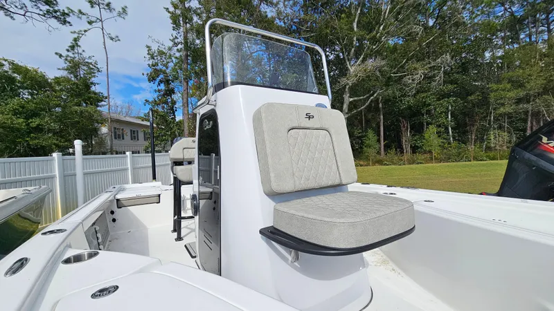 Slide: The Image of 2024 Sea Pro 210 Bay boat interior with seating and console, surrounded by trees and fencing. - 3