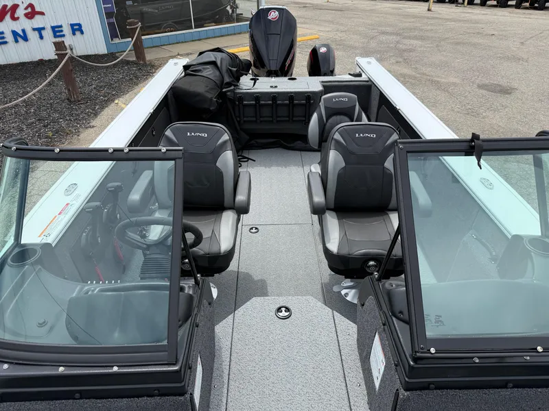 Slide: The Image of 2025 Lund Fisherman 2075 boat interior with seating and windshield, parked outdoors. - 11