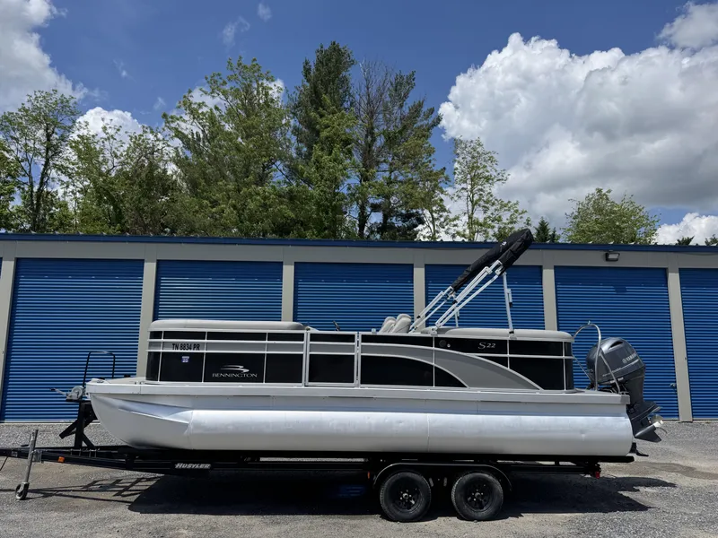 Slide: The Image of 2022 Bennington 22 SSR pontoon boat on trailer, parked by blue storage units. - 1