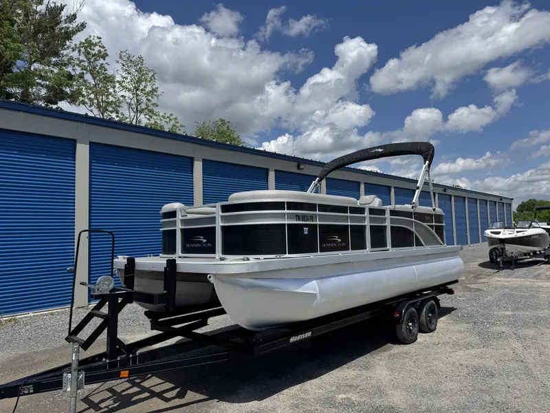 Slide: The Image of 2022 Bennington 22 SSR pontoon boat on trailer, parked near blue storage units. - 8