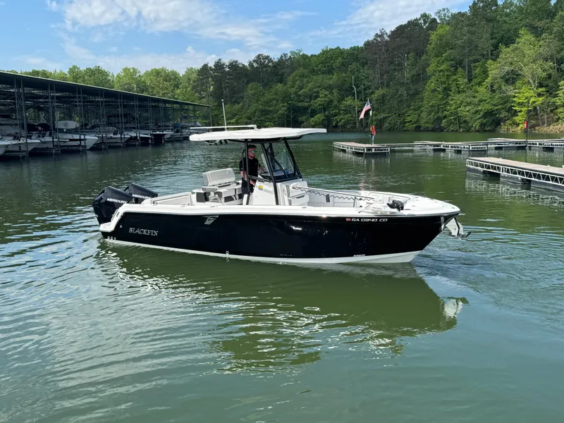 Slide: The Image of 2023 Blackfin 252 CC boat on a calm lake near a marina, surrounded by lush greenery. - 3