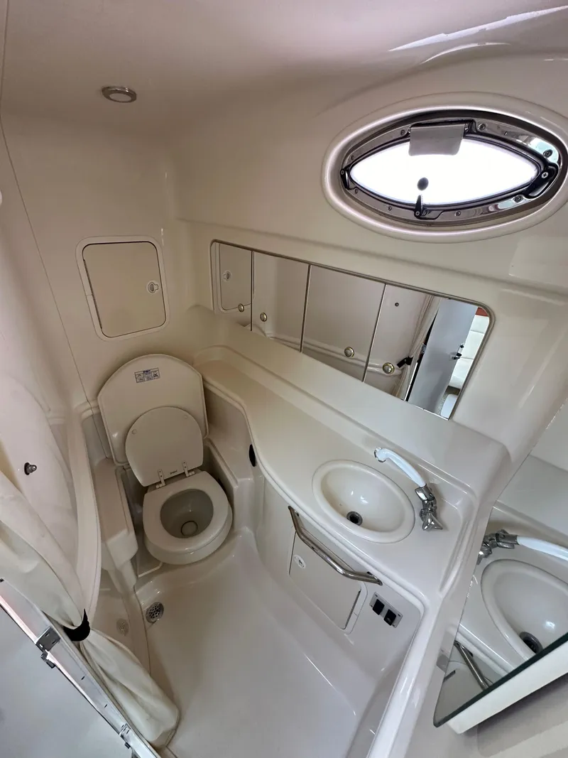 Slide: The Image of 2003 Sea Ray 320 Sundancer bathroom with toilet, sink, mirror, and porthole window. - 30