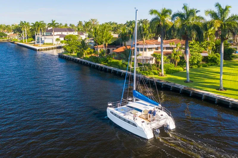 Slide: The Image of Catamaran sailing on a sunny canal near luxury waterfront homes and palm trees. - 9
