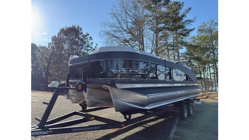 Slide: The Image of 2025 Tahoe Pontoon Cascade Cruise Rear Bench on trailer, parked near trees. - 3