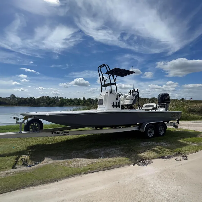 The Image of 2025 Tidewater 25 TPC Raptor boat on trailer by a lake under a blue sky. - 0