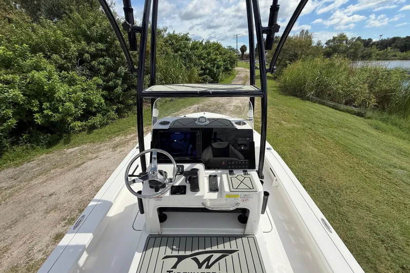 Slide: The Image of 2025 Tidewater 25 TPC Raptor boat console with steering wheel and controls, surrounded by greenery. - 16