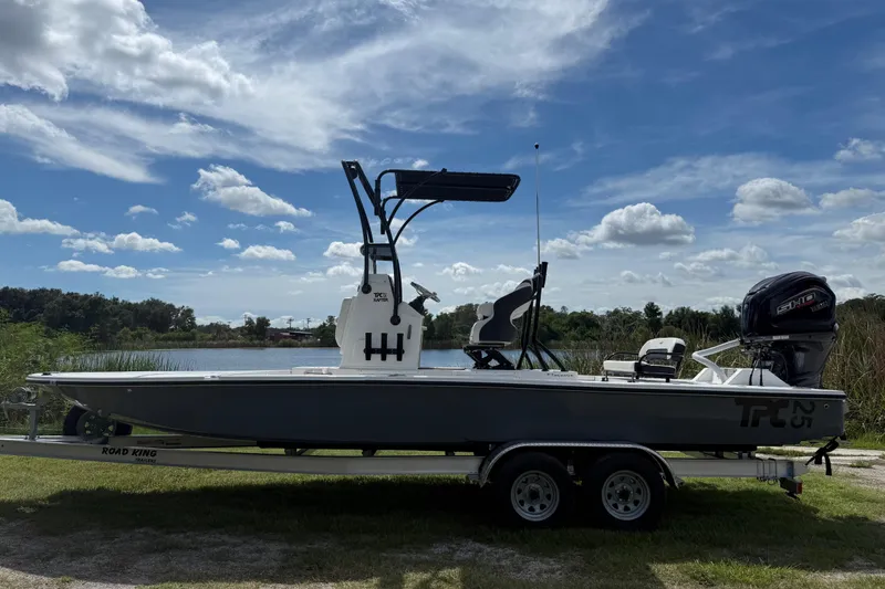 Slide: The Image of 2025 Tidewater 25 TPC Raptor boat on trailer by a lake under a blue sky. - 2